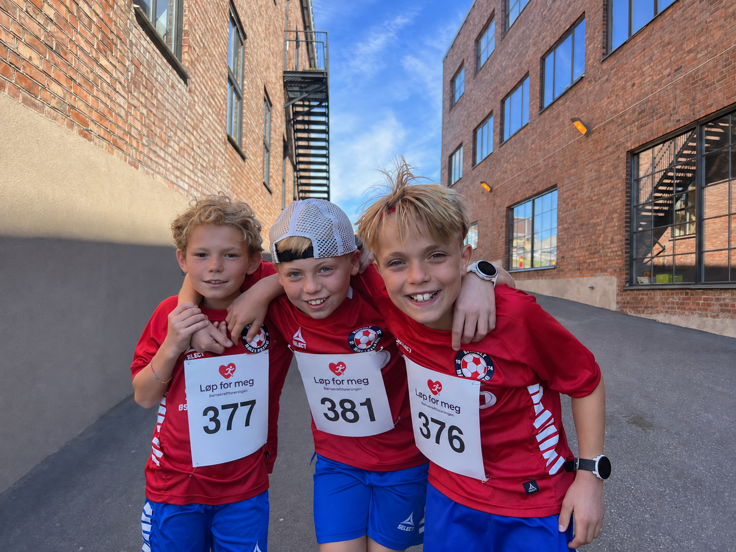 Tre unge løpere i røde trøyer lener seg over sperringen før start